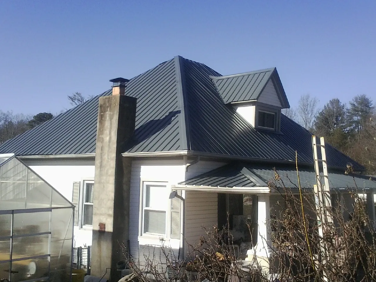 Dark blue standing seam metal roof on a white farmhouse with dormer — Slate & Tile Roof Repair by Roofing Brothers in Mount Pleasant